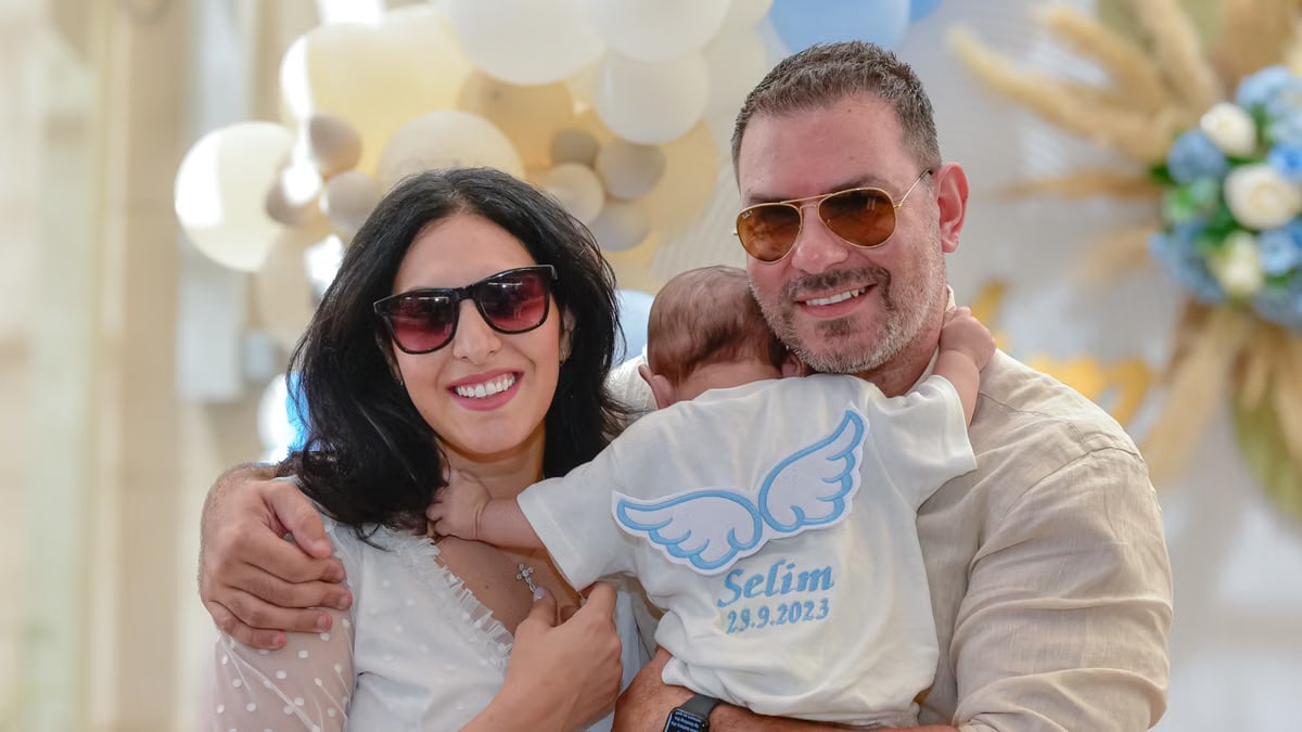 A joyful family celebrating a special occasion with their baby wearing an angel-themed shirt.