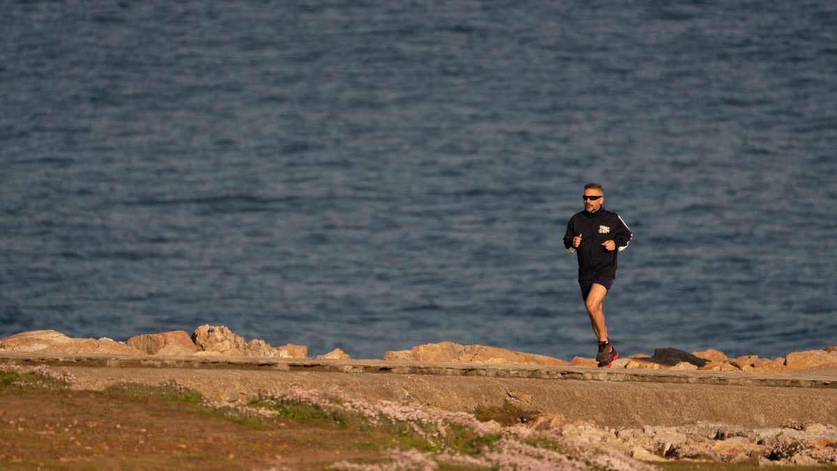 A man runs along a rocky shore with ocean in the background, showcasing fitness and tranquility.